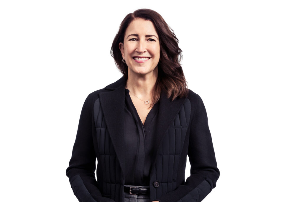 Smiling woman in a black blazer, standing against a plain white background.