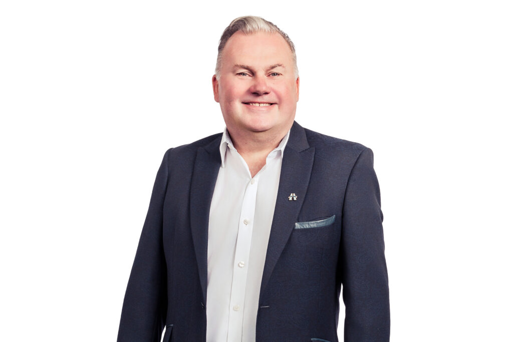 Smiling man in a dark blazer over a white shirt, standing against a white background.